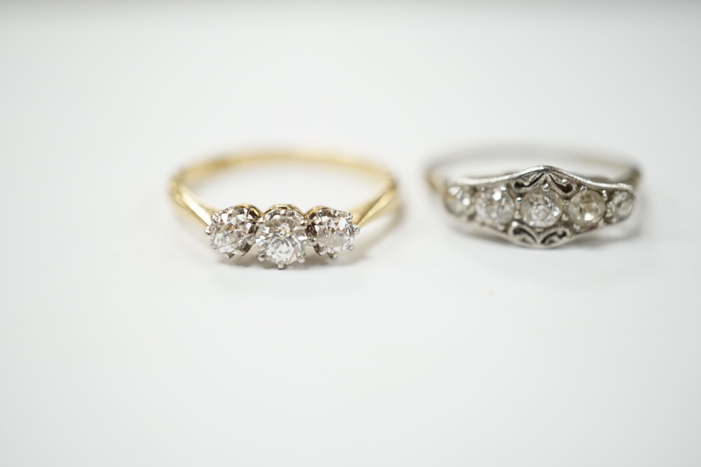 An 18ct gold three stone diamond ring, size M and a white metal five stone diamond dress ring, size M